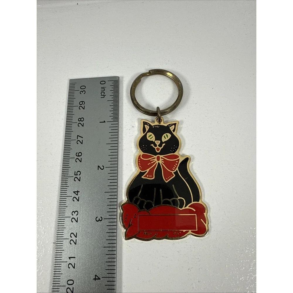 Black cat enamel keychain with gold-toned metal accents and‎ a red bow